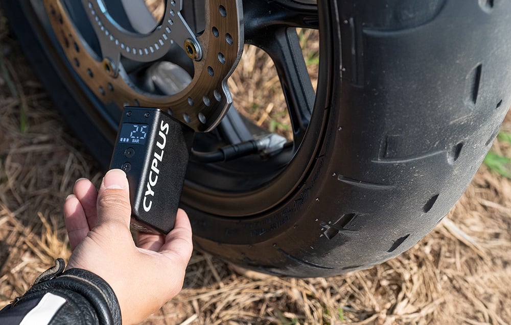Dłoń dociskająca czarną pompkę Cycplus do wentyla masywnego koła motocyklowego wyposażonego w tarczę hamulcową.